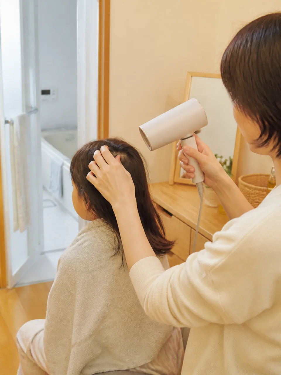 親が子どもの髪を指で分け、ドライヤーを離して根元から乾かす様子