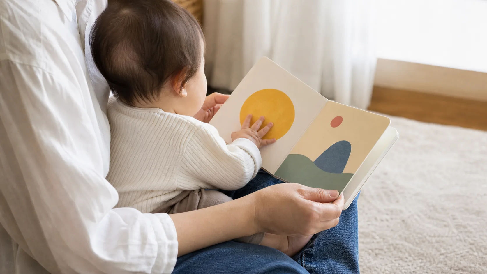 赤ちゃんを膝にのせて絵本を読み聞かせる手元